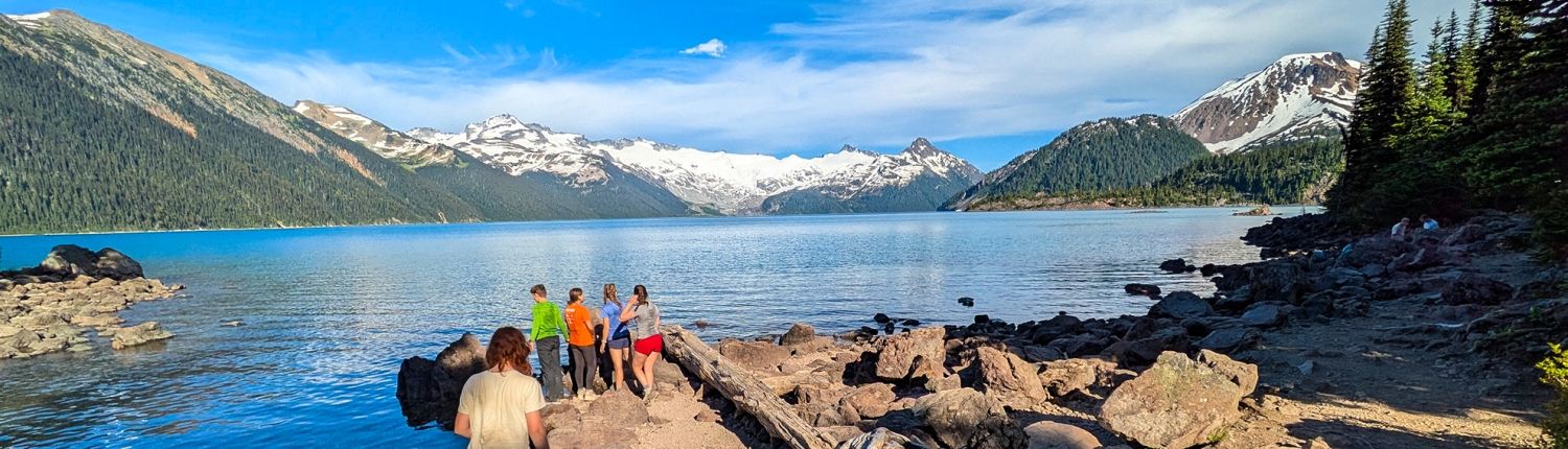 teenage boys and girls hanging out at a turquoise-colored lake in garibaldi provincial park in british columbia during teen summer camp