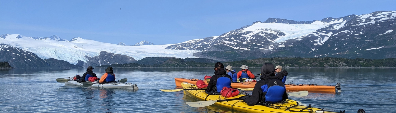 Teenagers and adults sea kayaking in Alaska's Prince William Sound with glaciers in the background