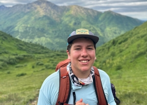 teenage boy in blue shirt and hat and neck buff hiking in alaska