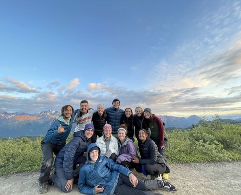 Group of teenage boys and girls smiling together on a trail in Alaska in front of a sunset