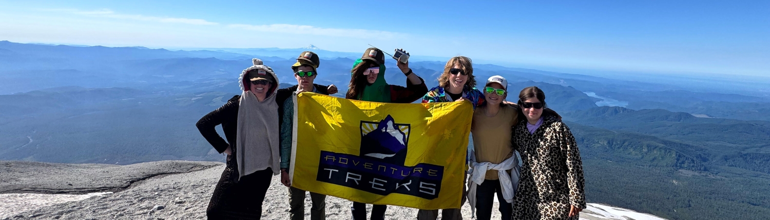 PNWA1-25-(11)-banner Teenagers standing atop the summit of Mount St. Helens with a yellow Adventure Treks flag