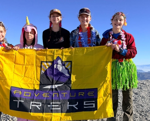 Teenagers standing atop the summit of Mount St. Helens with a yellow Adventure Treks flag